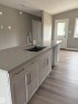 Kitchen featuring white cabinetry, light wood-style floors, a center island with sink, light stone counters, and lofted ceiling - 7413 44 Avenue, Camrose, AB  - Indoor Photo Showing Kitchen With Double Sink 