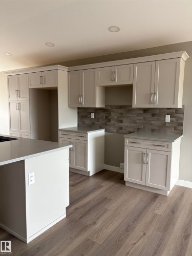 Kitchen with light wood finished floors, light stone counters, backsplash, white cabinetry, and recessed lighting - 7413 44 Avenue, Camrose, AB - Indoor Photo Showing Kitchen