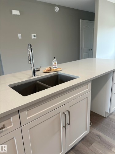 Kitchen with white cabinetry, light stone countertops, and light wood-style flooring - 7413 44 Avenue, Camrose, AB - Indoor Photo Showing Kitchen With Double Sink