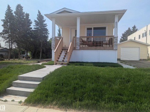View of front facade with an outdoor structure, a porch, a detached garage, stairway, and a front yard - 4921 50 Avenue, Legal, AB - Outdoor With Deck Patio Veranda