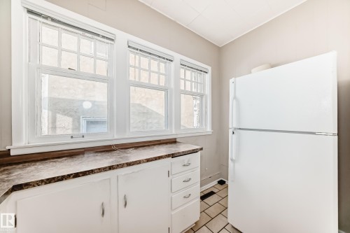 Kitchen with freestanding refrigerator, dark countertops, white cabinets, and light tile patterned flooring - 12605 107 Avenue, Edmonton, AB - Indoor