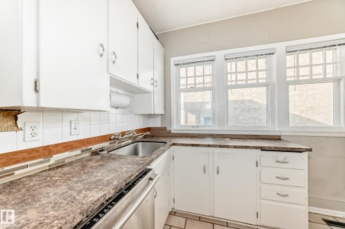 Kitchen featuring white cabinetry, stainless steel dishwasher, tasteful backsplash, dark countertops, and light tile patterned floors - 12605 107 Avenue, Edmonton, AB - Indoor Photo Showing Kitchen