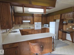 Kitchen featuring a kitchen breakfast bar, a peninsula, white appliances, backsplash, and brown cabinets - 