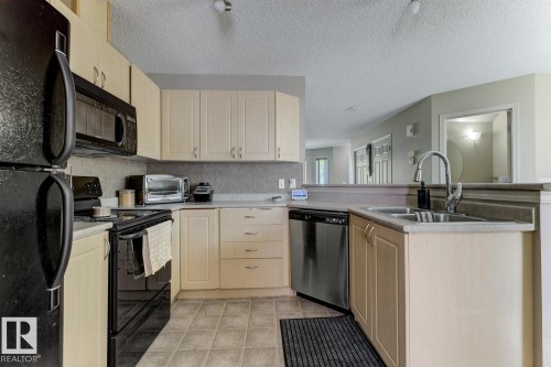 Kitchen with light brown cabinets, black appliances, tasteful backsplash, a peninsula, and a textured ceiling - 18 5281 Terwillegar Boulevard, Edmonton, AB - Indoor Photo Showing Kitchen With Double Sink