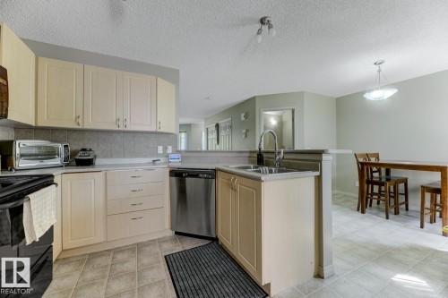 Kitchen featuring black electric range oven, dishwasher, light brown cabinetry, a peninsula, and a textured ceiling - 18 5281 Terwillegar Boulevard, Edmonton, AB - Indoor Photo Showing Kitchen With Double Sink