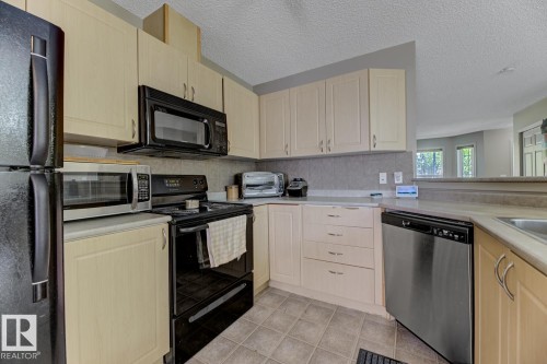 Kitchen with black appliances, light brown cabinetry, a textured ceiling, light countertops, and light tile patterned floors - 18 5281 Terwillegar Boulevard, Edmonton, AB - Indoor Photo Showing Kitchen