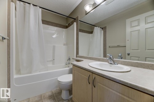 Bathroom with a textured ceiling, vanity, shower / bath combo with shower curtain, and tile patterned flooring - 18 5281 Terwillegar Boulevard, Edmonton, AB - Indoor Photo Showing Bathroom