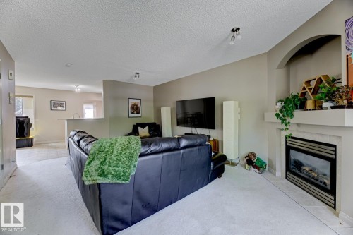 Living area featuring a textured ceiling, a tiled fireplace, and light colored carpet - 18 5281 Terwillegar Boulevard, Edmonton, AB - Indoor Photo Showing Living Room With Fireplace