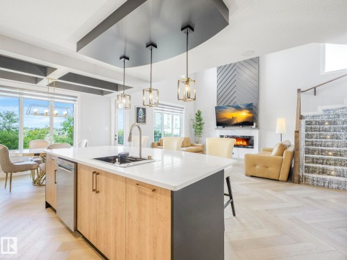 Kitchen with an island with sink, a large fireplace, open floor plan, a chandelier, and modern cabinets - 15 Elwyck Gate, Spruce Grove, AB - Indoor Photo Showing Kitchen