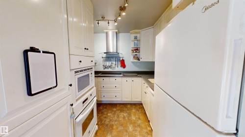 Kitchen with white appliances, wall chimney range hood, white cabinetry, and dark countertops - 3 Gold Eye Drive, Devon, AB - Indoor Photo Showing Kitchen