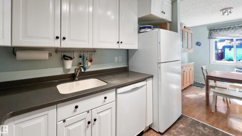 Kitchen featuring white appliances, a textured ceiling, white cabinets, dark countertops, and wood finished floors - 3 Gold Eye Drive, Devon, AB - Indoor Photo Showing Kitchen