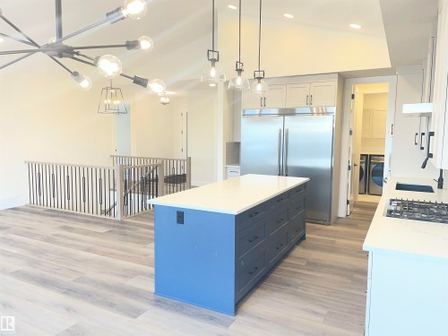 Two tone kitchen with dual tone cabinetry, decorative light fixtures, vaulted ceiling, a center island, and stainless steel appliances - 4112 Ginsburg Place, Edmonton, AB - Indoor Photo Showing Kitchen With Upgraded Kitchen