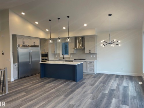 Kitchen featuring built in appliances, backsplash, a kitchen island, two tone cabinets, and dark wood-style flooring - 4112 Ginsburg Place, Edmonton, AB - Indoor Photo Showing Kitchen With Upgraded Kitchen