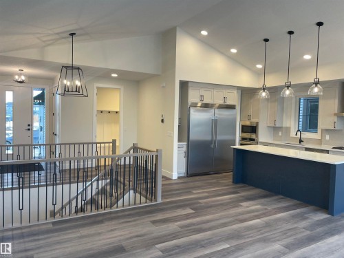 Dual tone kitchen featuring built in appliances, vaulted ceiling, dark wood-type flooring, a kitchen island, and hanging lights - 4112 Ginsburg Place, Edmonton, AB - Indoor Photo Showing Kitchen With Upgraded Kitchen