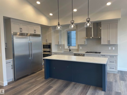 Kitchen with built in appliances, pendant lighting, light stone countertops, a kitchen island, and dark wood-type flooring - 4112 Ginsburg Place, Edmonton, AB - Indoor Photo Showing Kitchen With Upgraded Kitchen