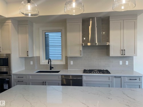 Kitchen with light stone countertops, tasteful backsplash, stainless steel appliances, and white cabinetry - 4112 Ginsburg Place, Edmonton, AB - Indoor Photo Showing Kitchen With Upgraded Kitchen