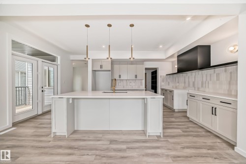 Kitchen featuring decorative backsplash, an island with sink, light wood-style flooring, pendant lighting, and light countertops - 1401 Ainslie Wynd, Edmonton, AB - Indoor Photo Showing Kitchen