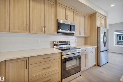 Kitchen with light brown cabinets, appliances with stainless steel finishes, decorative backsplash, light stone counters, and recessed lighting - 9104 Elves Loop, Edmonton, AB - Indoor Photo Showing Kitchen