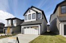 Modern farmhouse style home featuring an attached garage, board and batten siding, a shingled roof, concrete driveway, and a front lawn - 9104 Elves Loop, Edmonton, AB  - Outdoor 