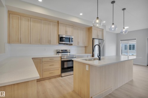 Kitchen with light brown cabinetry, stainless steel appliances, decorative backsplash, light stone countertops, and a kitchen island with sink - 9104 Elves Loop, Edmonton, AB - Indoor Photo Showing Kitchen With Upgraded Kitchen