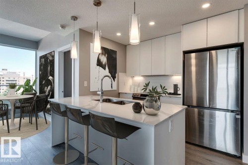 Kitchen featuring freestanding refrigerator, light stone countertops, a textured ceiling, a kitchen breakfast bar, and light wood-style floors - 9922 111 Street, Edmonton, AB - Indoor Photo Showing Kitchen With Stainless Steel Kitchen With Double Sink With Upgraded Kitchen