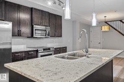 Kitchen with backsplash, appliances with stainless steel finishes, light stone countertops, light wood-style flooring, and decorative light fixtures - 