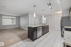 Kitchen featuring an island with sink, dishwasher, light tile patterned floors, hanging light fixtures, and light stone counters - 