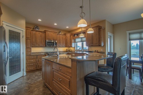 Kitchen featuring brown cabinetry, a breakfast bar, dark stone countertops, stainless steel appliances, and pendant lighting - 5753 43 Ave, St. Paul Town, AB - Indoor Photo Showing Kitchen With Double Sink