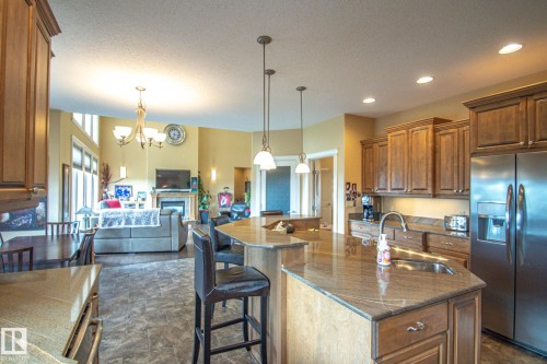 Kitchen with stainless steel refrigerator with ice dispenser, a breakfast bar, brown cabinetry, a chandelier, and stone finish floors - 5753 43 Ave, St. Paul Town, AB - Indoor Photo Showing Kitchen