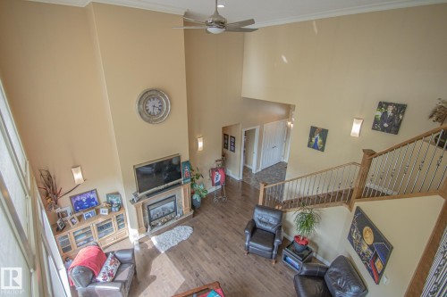 Living room featuring stairway, wood finished floors, a high ceiling, crown molding, and a ceiling fan - 5753 43 Ave, St. Paul Town, AB - Indoor With Fireplace