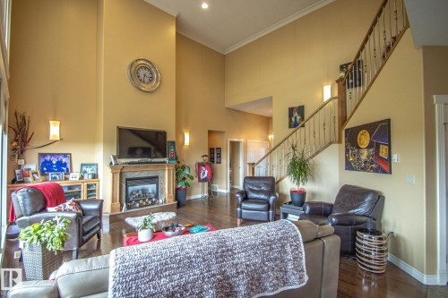 Living area with dark wood-type flooring, ornamental molding, a fireplace, stairs, and a high ceiling - 5753 43 Ave, St. Paul Town, AB - Indoor With Fireplace