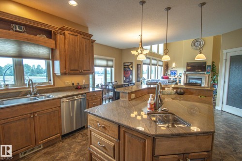 Kitchen with brown cabinets, decorative light fixtures, stainless steel dishwasher, open floor plan, and a kitchen island with sink - 5753 43 Ave, St. Paul Town, AB - Indoor Photo Showing Kitchen With Double Sink