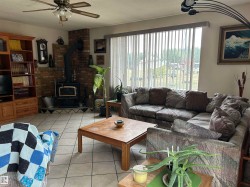 Living area featuring a wood stove, a ceiling fan, light tile patterned flooring, and a textured ceiling - 