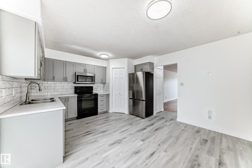 Kitchen featuring stainless steel appliances, gray cabinets, tasteful backsplash, light wood-style flooring, and a textured ceiling - 13116 31 Strret, Edmonton, AB - Indoor Photo Showing Kitchen With Double Sink