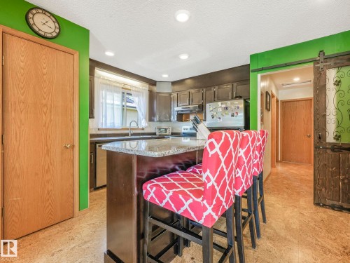 Kitchen Upgraded counters, a textured ceiling, dark brown cabinetry, center island c/w Breakfast Bar. - 3608 15 Avenue, Edmonton, AB - Indoor
