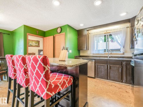 Kitchen featuring a textured ceiling, a kitchen bar, appliances with stainless steel finishes, a center island, and dark brown cabinetry - 3608 15 Avenue, Edmonton, AB - Indoor