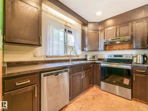 Kitchen featuring stainless steel appliances, under cabinet range hood, a textured ceiling, and dark brown cabinetry - 3608 15 Avenue, Edmonton, AB - Indoor Photo Showing Kitchen