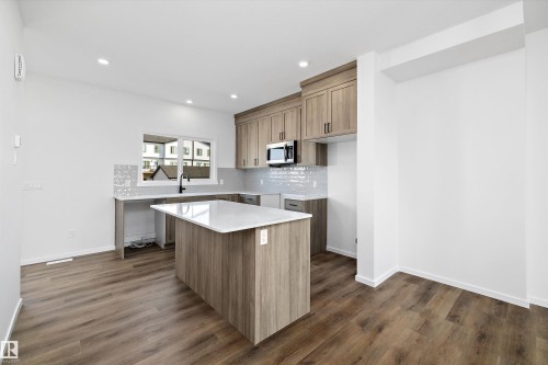 Kitchen with decorative backsplash, brown cabinetry, light stone counters, dark wood-style flooring, and recessed lighting - 5458 Hawthorn Run, Edmonton, AB - Indoor Photo Showing Kitchen