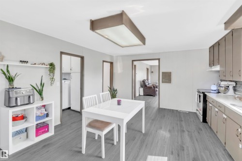 Kitchen featuring light wood-style flooring, light countertops, stainless steel electric stove, under cabinet range hood, and washer / dryer - 4702 50 Avenue, Cold Lake, AB - Indoor