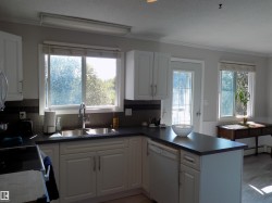 Kitchen featuring a peninsula, white cabinets, white dishwasher, dark countertops, and decorative backsplash - 