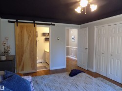 Bedroom featuring wood finished floors, a closet, ceiling fan, baseboard heating, and a barn door - 