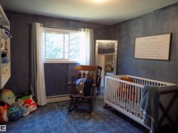 Bedroom featuring a crib, a textured ceiling, dark carpet, and a baseboard radiator - 