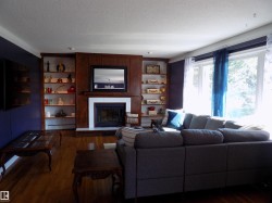 Living area with a textured ceiling, wood finished floors, a large fireplace, built in shelves, and ornamental molding - 