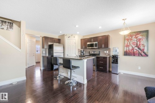 Kitchen with dark brown cabinetry, a kitchen breakfast bar, appliances with stainless steel finishes, dark wood-type flooring, and recessed lighting - 6819 Cardinal Link, Edmonton, AB - Indoor Photo Showing Kitchen With Upgraded Kitchen