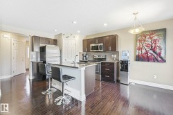 Kitchen with dark brown cabinets, appliances with stainless steel finishes, a kitchen bar, light stone counters, and recessed lighting - 