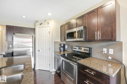 Kitchen with stainless steel appliances, dark brown cabinets, a textured ceiling, light stone countertops, and recessed lighting - 6819 Cardinal Link, Edmonton, AB - Indoor Photo Showing Kitchen With Double Sink With Upgraded Kitchen