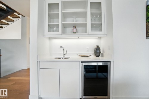 Indoor wet bar with white cabinets, beverage cooler, light stone counters, wood finished floors, and glass insert cabinets - 11823 Saskatchewan Drive, Edmonton, AB - Indoor