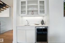 Indoor wet bar with white cabinets, beverage cooler, light stone counters, wood finished floors, and glass insert cabinets - 