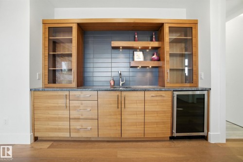 Indoor bar featuring modern cabinets, beverage cooler, backsplash, light wood-style flooring, and dark stone counters - 11823 Saskatchewan Drive, Edmonton, AB - Indoor