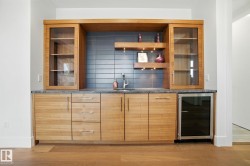 Indoor bar featuring modern cabinets, beverage cooler, backsplash, light wood-style flooring, and dark stone counters - 